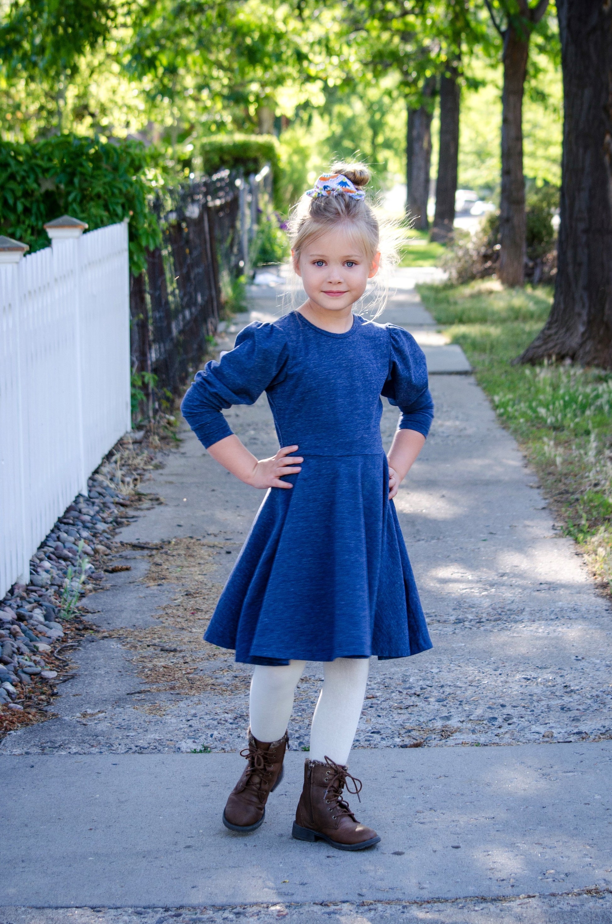 Girl in a blue dress posing on a sidewalk.