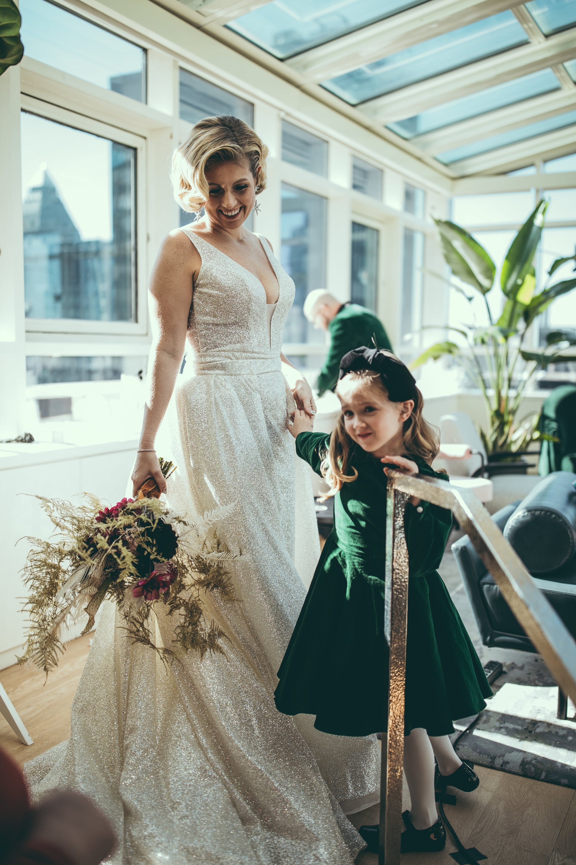 Flower girl in a green velvet dress standing next to a bride.
