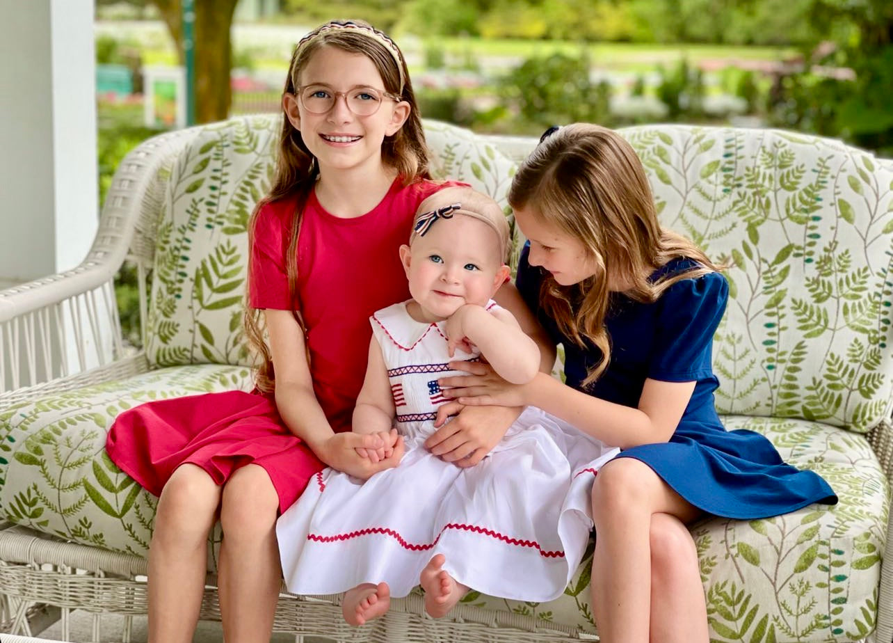 Three girls in cute dresses on a couch.